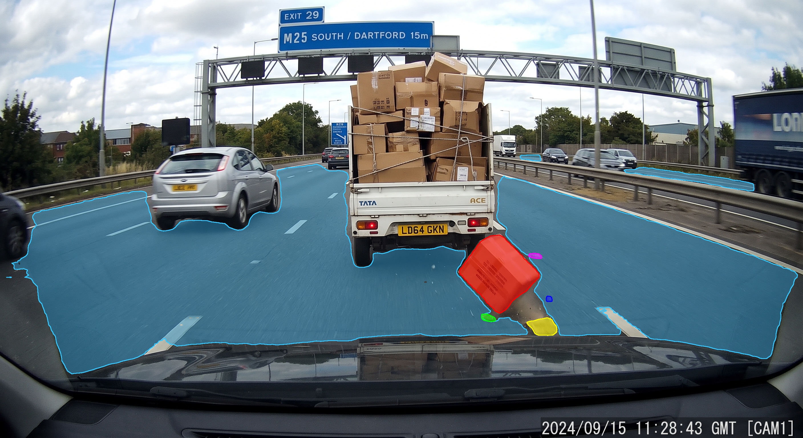 Dashcam frame on the M25: drivable road surface segmented in blue, cargo falling from a truck segmented as debris